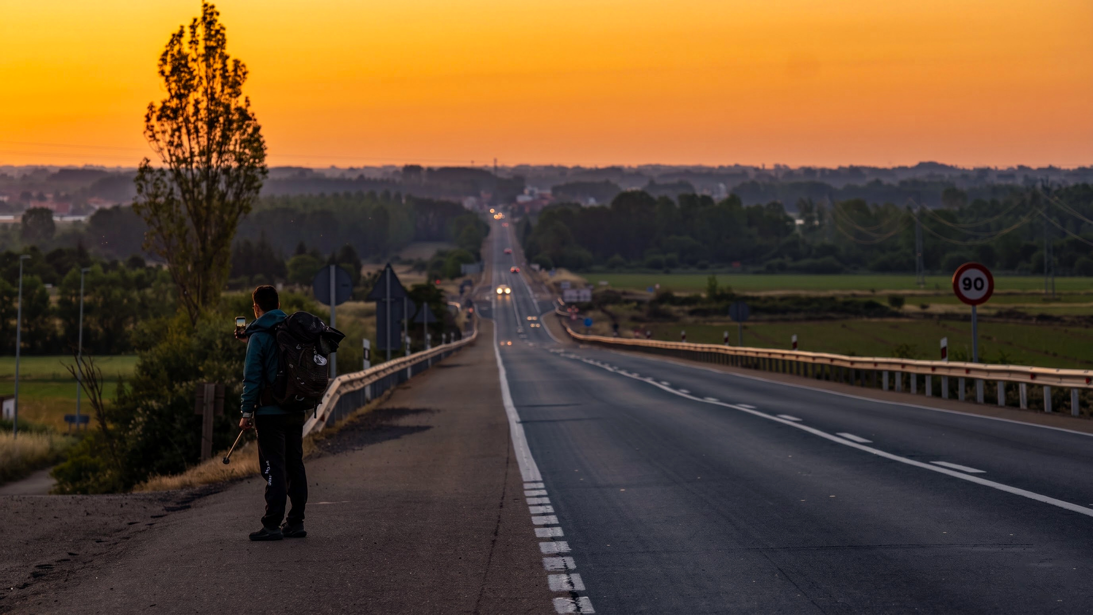 夕陽下公路上背著背包前行的朝聖者